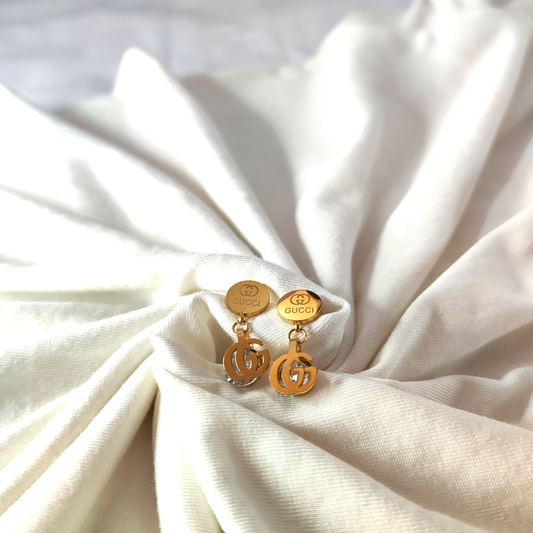 Gold earrings with a Gucci logo on a white fabric background